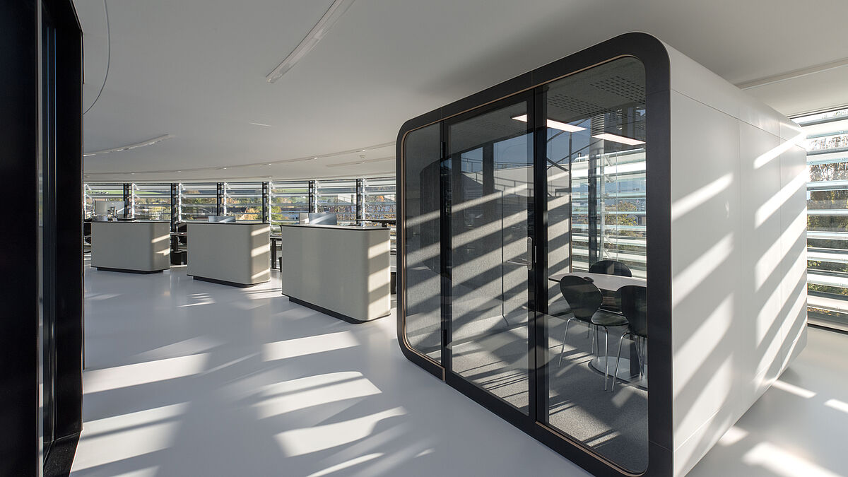 Sechs frei im Raum stehende, schallgedämpfte Besprechungsboxen ermöglichen den Mitarbeitenden Diskretion und Ruhe zugleich. Zudem gliedern sie die Räumlichkeiten. Bild: Zuzana Oplatek