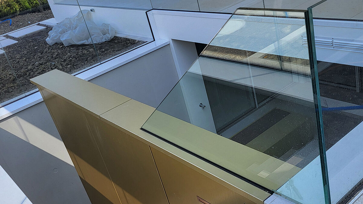 Äusserer Treppenabgang mit edlem Glasgeländer und verblechter Betonscheibe um den Treppenkern. Im Blech integrierte Leuchtkörper machen die Begehung bei Nacht sicher.     (Bild bei Bedarf im Print weglassen!)