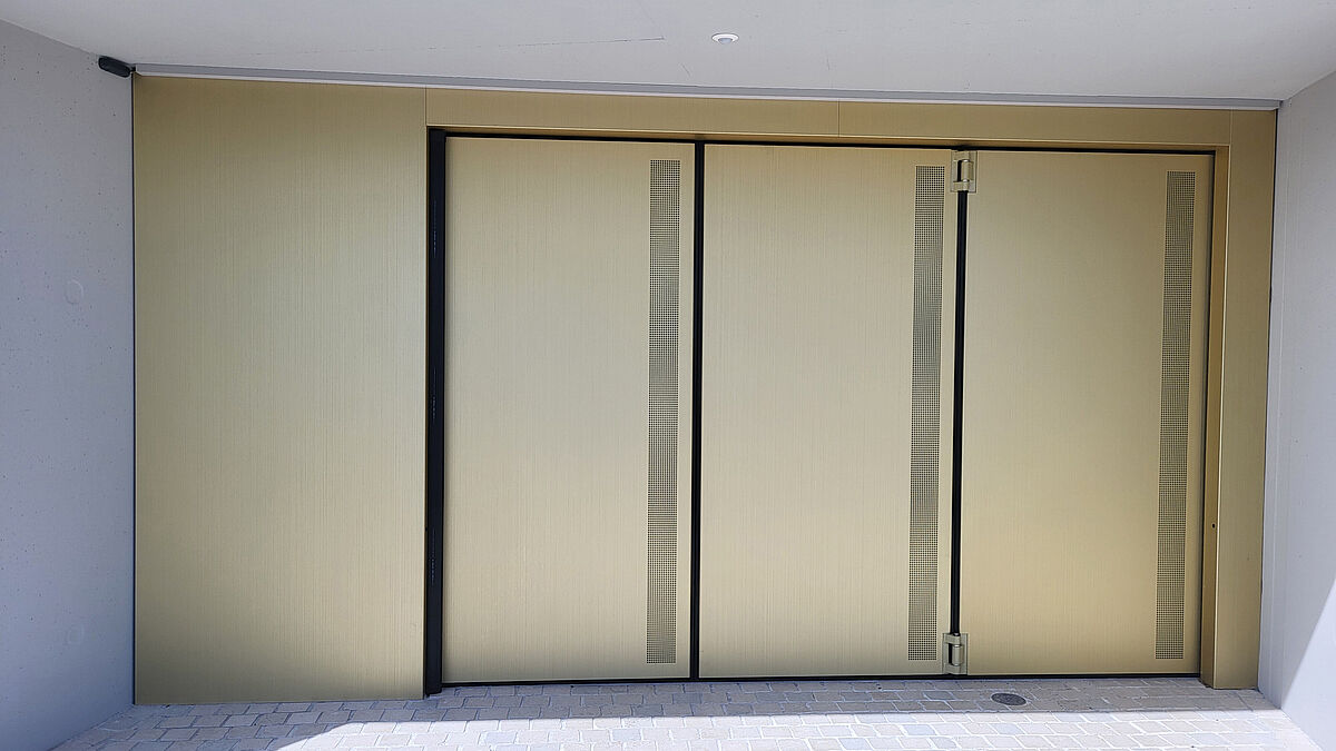 Die drei Flügelverkleidungen sind mit quadratischen, lasergeschnittenen Lochstreifen ausgeführt – eine optische und lüftungstechnische Lösung in Kombination.