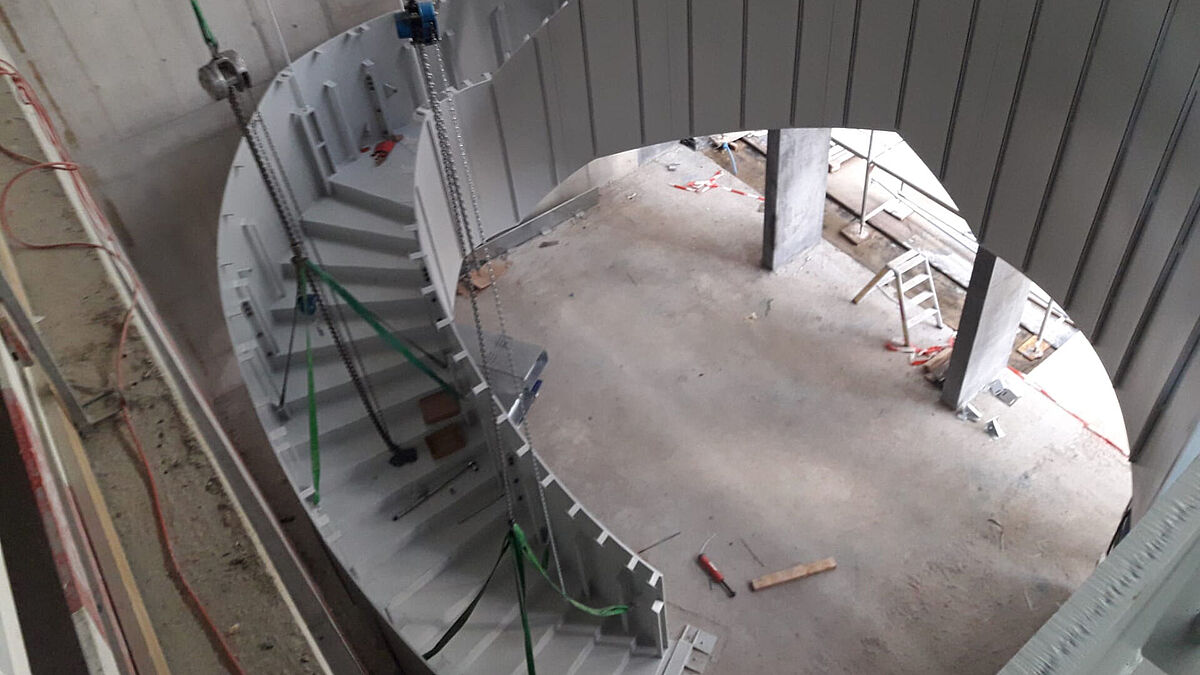 Montage der letzten Elemente im Erdgeschoss. Gut zu erkennen sind die verschiedenen Kettenzüge, welche die ganze Anlage provisorisch tragen, bis alle Elemente miteinander steif verschraubt und die vier Zugstangen angebracht waren.