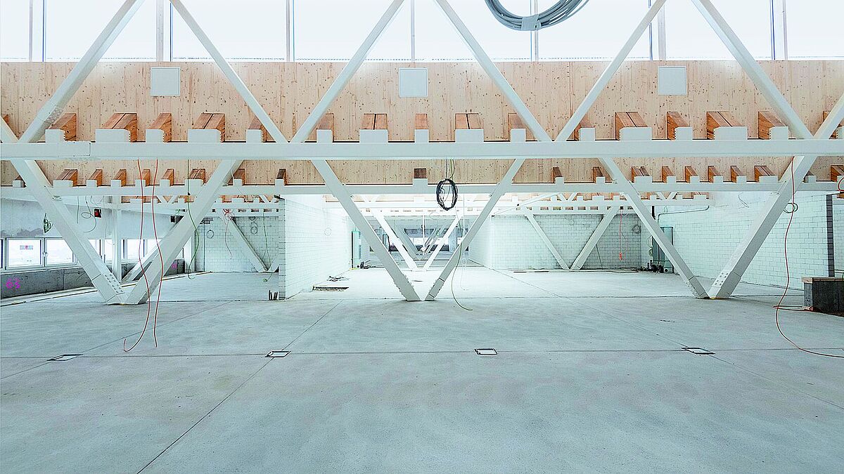 Die kleinen Fachwerkträger (vorn) tragen nur Teile des Dachs, die doppelstöckigen tragen dazu noch die Decke der Sporthalle und der Aula.