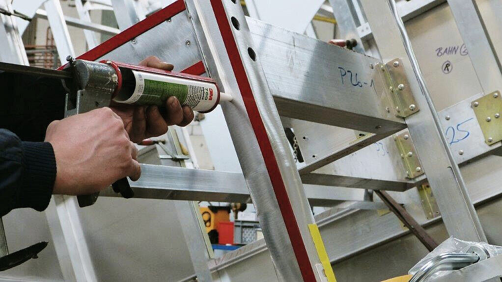 Bild IBZ. Vorbereitung Kombiklebung: Doppelseitiges Montageklebeband wird aufgeklebt und mit der Anpressrolle angedruckt. Die Klebe-Dichtmasse wird neben dem Klebeband aufgetragen. 