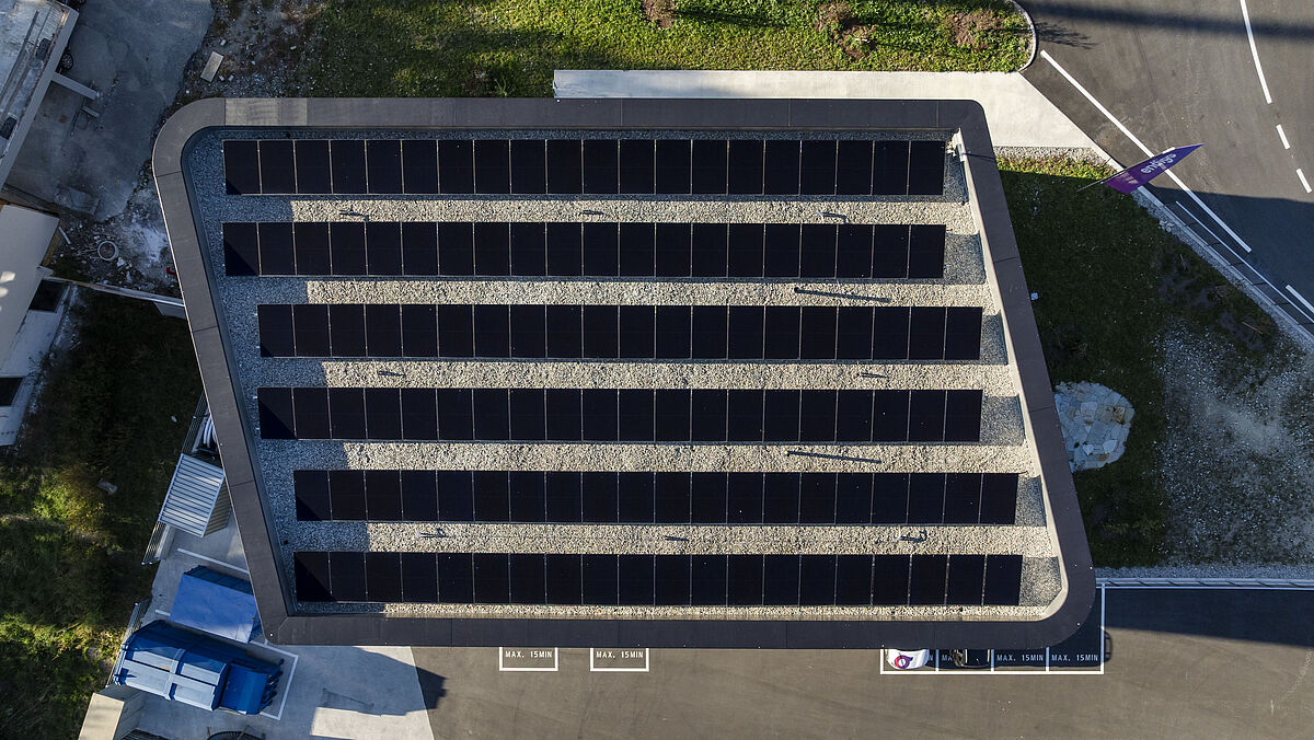 Draufsicht: Der trapezförmige Grundriss mit zwei in einem grosszügigen Radius verlaufenden Ecken. Das Flachdach ist ebenfalls mit PV-Modulen belegt.