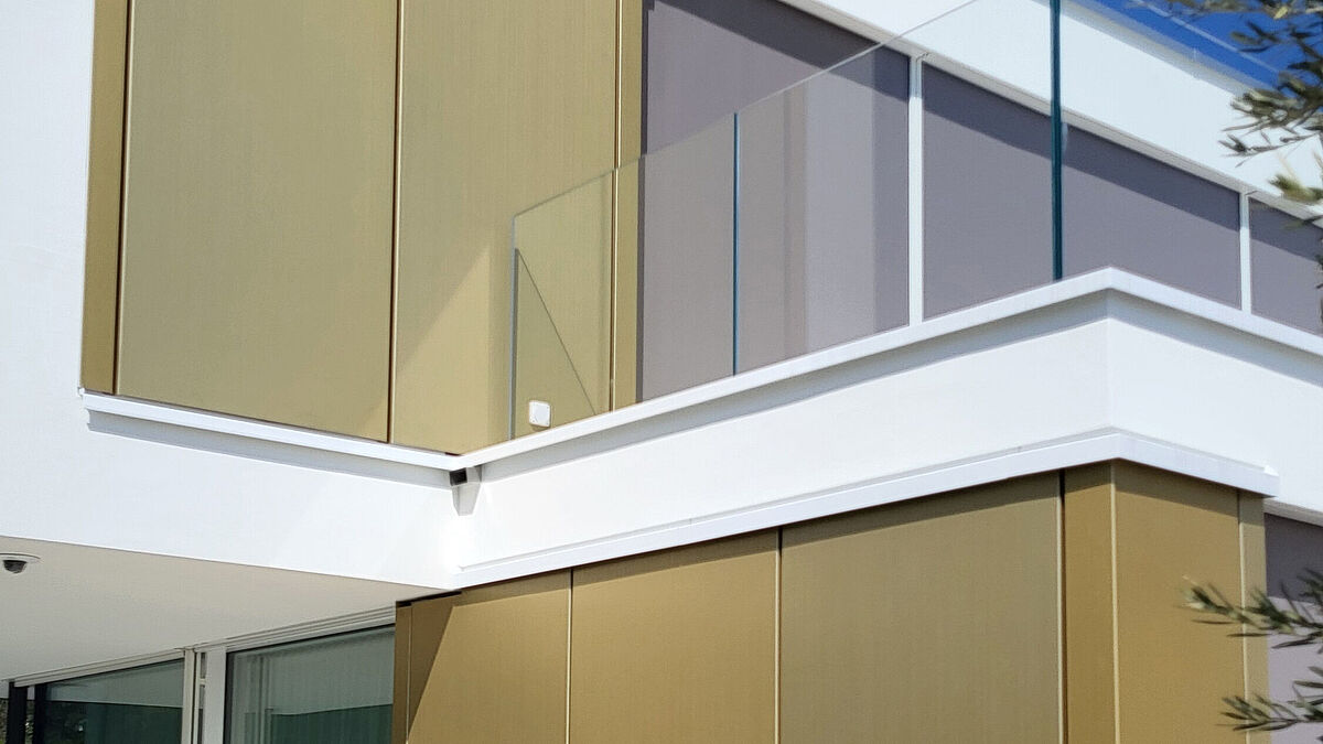 Eine gelungene optische Kombination zwischen der beigen, verputzten Fassade, den goldenen Aluminiumblechen und dem kristallfarbigen Glas.    (Bild bei Bedarf im Print weglassen!)