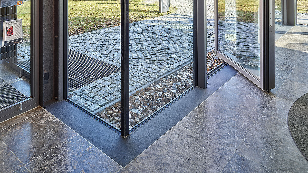 Vue des angles en verre depuis l’intérieur. À côté, une porte pivotante à un vantail.