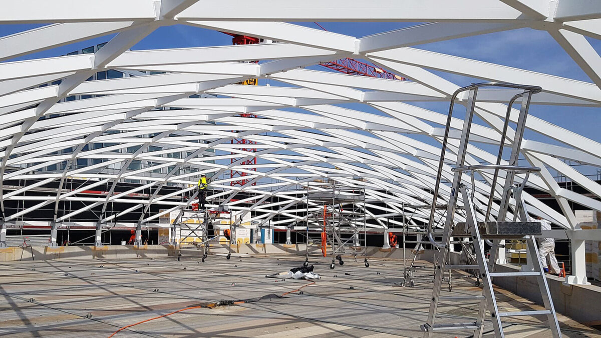 Montagephase: Das Gitterstrukturdach ruht auf einer Sockelmauer. Auf dieser ist ein umlaufender Stahl-Randträger aufgeständert, welcher der Dachkonstruktion als Widerlager resp. als Druckring dient. 